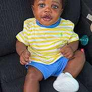 Sameir joined the competition — help win amazing prizes! baby, child, car_seat, striped_shirt, yellow, blue_shorts, white_sneakers, happy, smiling, person, indoor, clothing, footwear, cute, seated, infant, curious, black_hair, skin, portrait
