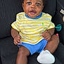 baby, child, car_seat, striped_shirt, yellow, blue_shorts, white_sneakers, happy, smiling, person, indoor, clothing, footwear, cute, seated, infant, curious, black_hair, skin, portrait