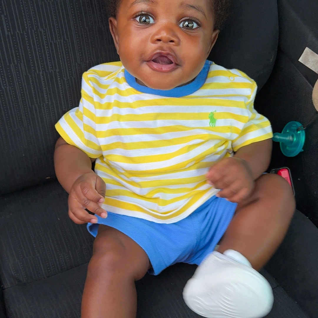 Sameir joined the competition — help win amazing prizes! baby, black_hair, blue_shorts, car_seat, child, clothing, curious, cute, footwear, happy, indoor, infant, person, portrait, seated, skin, smiling, striped_shirt, white_sneakers, yellow