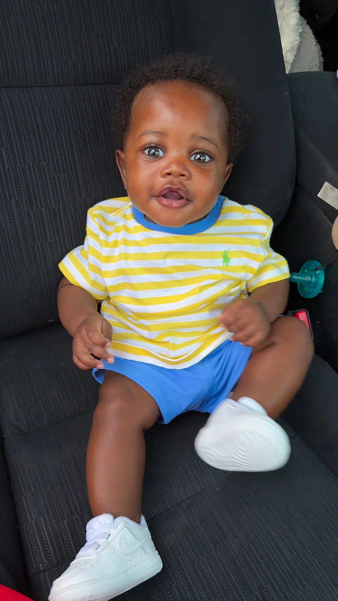 Sameir joined the competition — help win amazing prizes! baby, child, car_seat, striped_shirt, yellow, blue_shorts, white_sneakers, happy, smiling, person, indoor, clothing, footwear, cute, seated, infant, curious, black_hair, skin, portrait