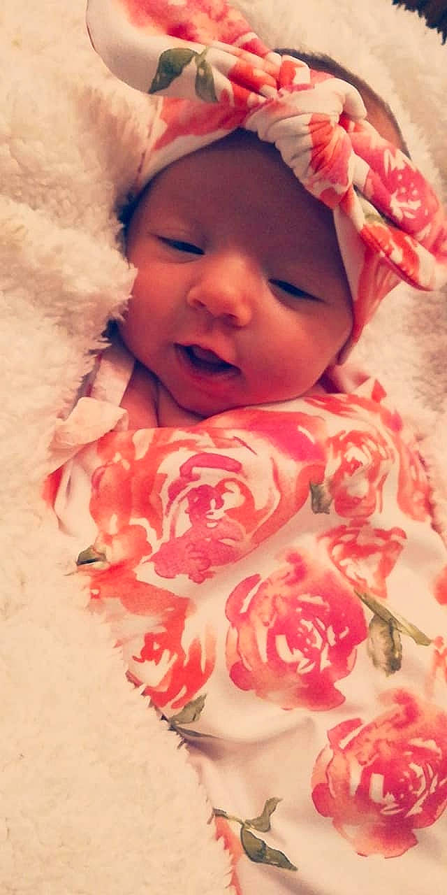 Ember is registered to the contest to win money with this photo: baby, cheek, child, eye, face, facial_expression, flower, hair_accessory, head, headgear, lip, mouth, nose, person, petal, pink, skin, smile, toddler