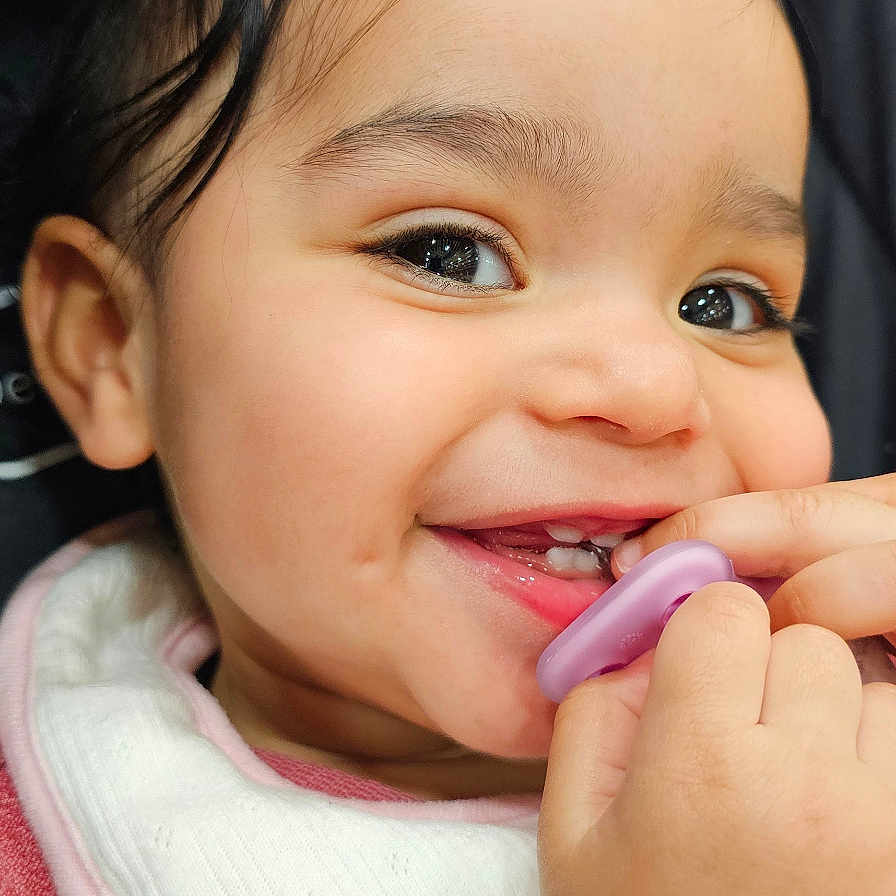 Raniyah joined the competition — help win amazing prizes! baby, child, toddler, smiling, happy, portrait, close_up, face, eyes, teeth, pacifier, hand, adult_hand, bib, clothing, pink, purple, seated, car_seat, indoor