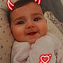 adorable, baby, blanket, child, closeup, cozy, cute, devil_horns, digital_sticker, face, happy, heart_arrow, indoors, infant, pillow, portrait, sleepwear, smiling, soft_lighting, warm
