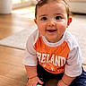 baby, bright, casual_clothing, child, cute, floor, happy, home, indoor, natural_light, orange_shirt, person, pigtails, portrait, sitting, smiling, socks, white_shirt, wooden_floor, young_child