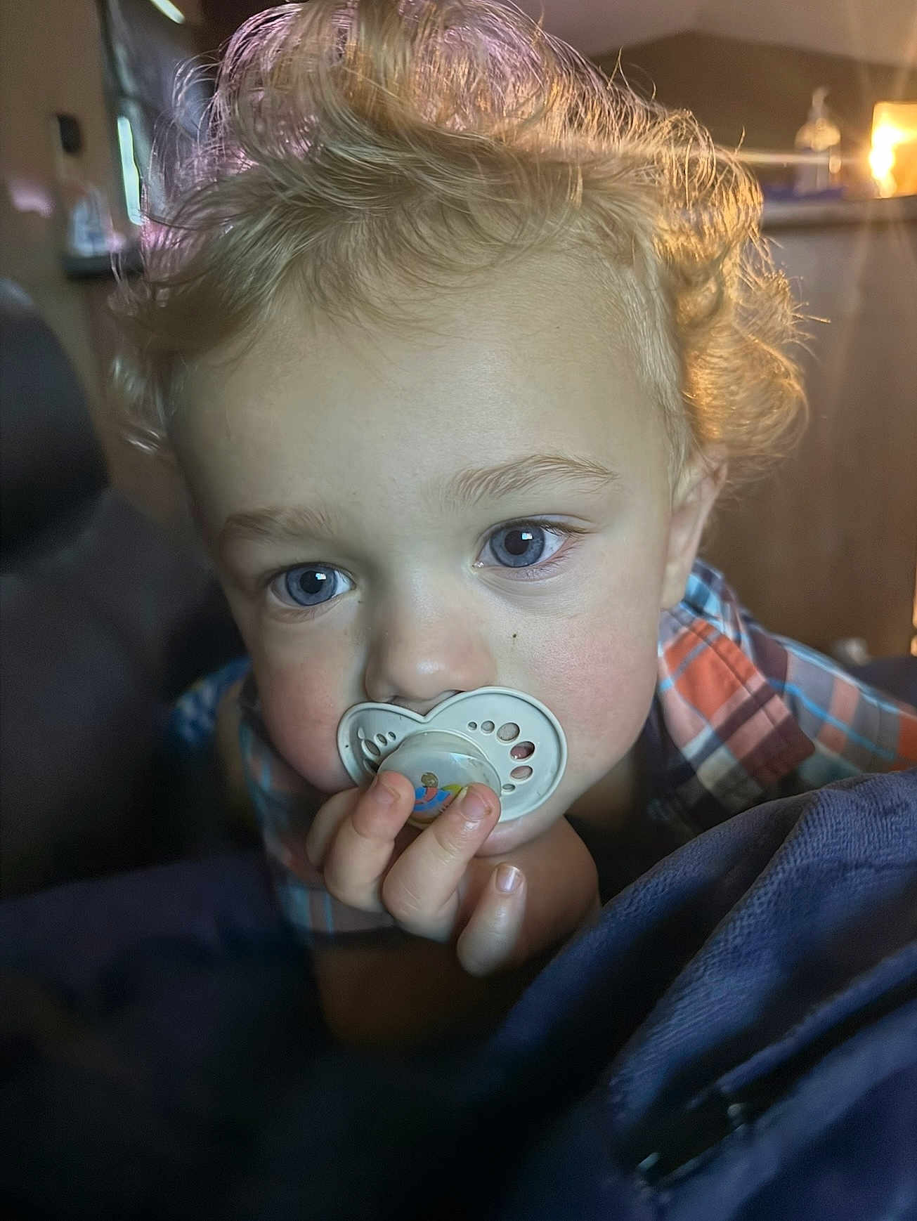 Dangelo is registered to the contest to win money with this photo: toddler, child, pacifier, curly_hair, blue_eyes, indoor, blanket, closeup, portrait, hand, face, young_child, cozy, curly, infant, plaid_shirt, cute, baby, indoor_lighting, soft_light