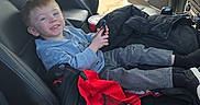 Liam joined the competition — help win amazing prizes! child, car_interior, seat, smiling, young_boy, casual_clothing, daylight, open_car_door, vehicle, parked_car, black_seat, happy, person, leisure, holding_object, window, jacket, footwear, red_bag, seatbelt