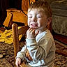 Liam is registered to the contest to win money with this photo: child, red_hair, wooden_chair, rocking_horse, living_room, carpet, sofa, sweatshirt, bear_graphic, smile, funny_face, indoor, person, furniture, wood, toy, cozy, casual_clothing, home, seated