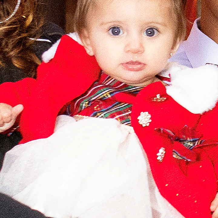 Dalylah is registered to the contest to win money with this photo: baby, blue_eyes, celebration, child, cute, family, fashion, festive_clothing, hands, holding, indoor, people, person, portrait, red_cardigan, smile, toddler, white_bow, white_dress, young_child