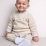 child, toddler, smile, sweater, knit_sweater, white_shoes, pants, striped_shirt, portrait, studio, indoor, cute, happy, sitting, face, ears, beige, minimalist_background, baby, clothing