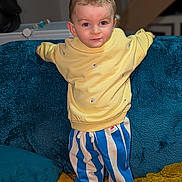 Swan participe au concours pour gagner de l'argent avec cette photo : child, toddler, yellow_sweater, striped_pants, blue_and_white_stripes, sofa, couch, blanket, pillow, indoor, portrait, standing, smiling, eyes, hair, cute, home_interior, fabric_texture, childrens_clothing, playful