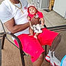 adult, baby, man, child, chair, clothing, sneakers, jewelry, outdoor, patio, floor, table, expression, person, hat, shorts, white_shirt, red_clothing, footwear, casual