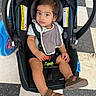 baby, bib, car_seat, casual_clothing, checkered_floor, child, curious, floor, footwear, indoor, person, portrait, safety, sandals, seat, seat_belt, striped_shirt, toddler, warning_label, young_child