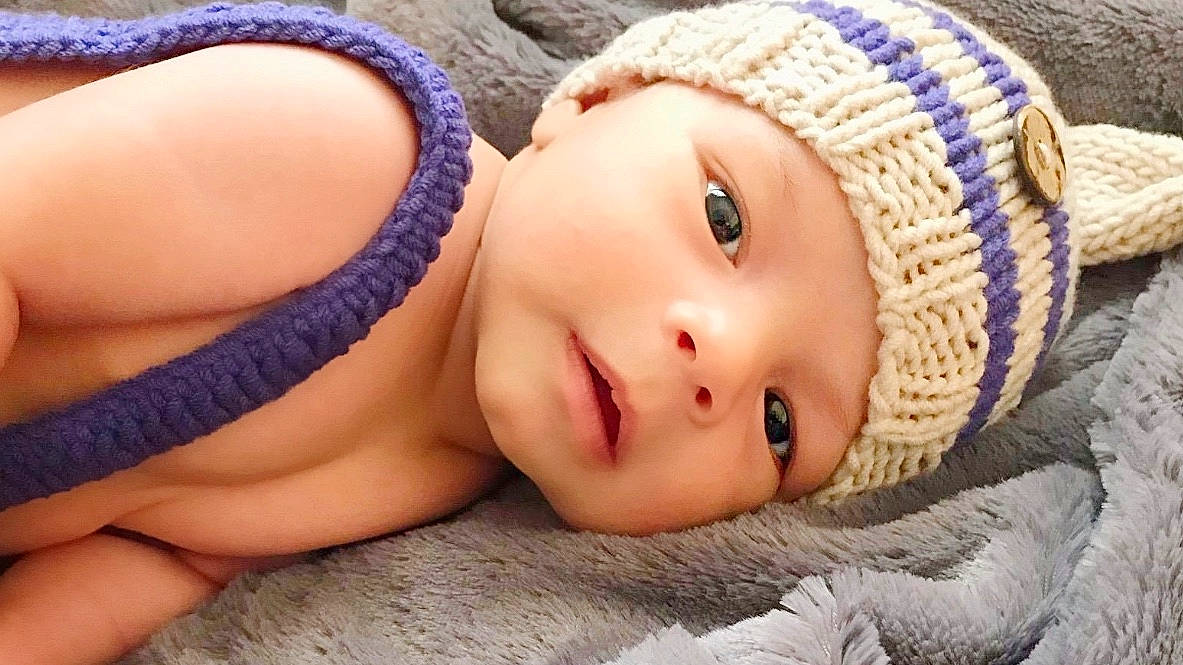 Seven is registered to the contest to win money with this photo: baby, beanie, beauty, cap, cheek, child, close_up, crochet, eye, face, head, headgear, headwear, knit_cap, lip, mouth, nose, person, photography, skin