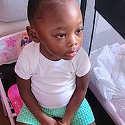 Armani joined the competition — help win amazing prizes! child, girl, hair_bow, curly_hair, white_shirt, green_shorts, sitting, pink_chair, toys, baby_shark, yellow_container, wooden_floor, indoor, casual_clothing, footwear, white_shoes, bracelet, playroom, thoughtful, portrait