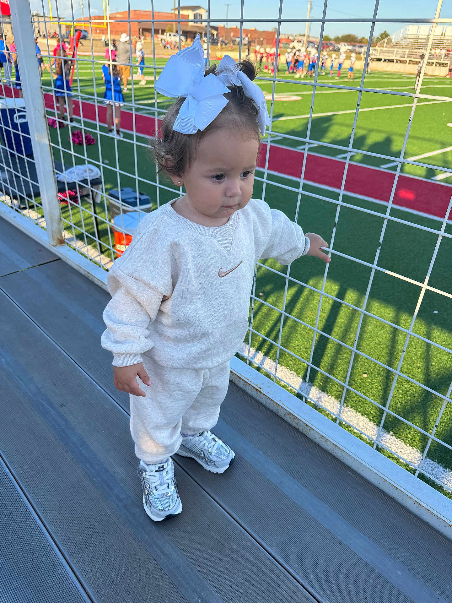 Fallyn joined the competition — help win amazing prizes! bleachers, casual_clothing, child, daylight, football_field, girl, green_field, nike, outdoor, shadows, sneakers, spectators, sports, stadium, sweatpants, sweatshirt, toddler, white_bows, wire_fence, young_child
