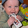 Jak is registered to the contest to win money with this photo: baby, blue_cap, chewing, child, clothing, colorful, cute, face, hands, happy, headwear, indoor, infant, penguin_patch, phone_case, playtime, portrait, smiling, toys, young_child