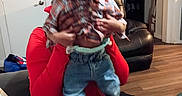 Melvin joined the competition — help win amazing prizes! toddler, child, adult, person, portrait, indoors, living_room, sitting, holding, plaid_shirt, jeans, red_shoes, sneakers, braids, smiling, family, furniture, couch, wood_floor, home