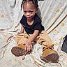 Melvin joined the competition — help win amazing prizes! child, toddler, portrait, sitting, bed, bedroom, floral, bedspread, boots, shoes, clothing, black_shirt, tan_pants, braided_hair, hairstyle, face, serious_expression, indoors, fashion, photography