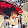 child, toddler, sleeping, stroller, outdoor, sunlight, portrait, face, baby, harness, seatbelt, wheelchair, wheels, red, blue, white, clothing, concrete, park, transportation
