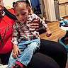 child, toddler, baby, sitting, being_held, adult, face, portrait, sleepy, indoor, home, kitchen, chair, plaid_shirt, jeans, red_shoes, sneakers, baby_walker, family, casual_clothing