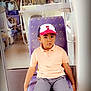 child, boy, train, seat, cap, spiderman, shorts, casual_clothing, indoor, public_transport, window, curious, sitting, purple_seat, young, person, travel, public_space, portrait, daylight