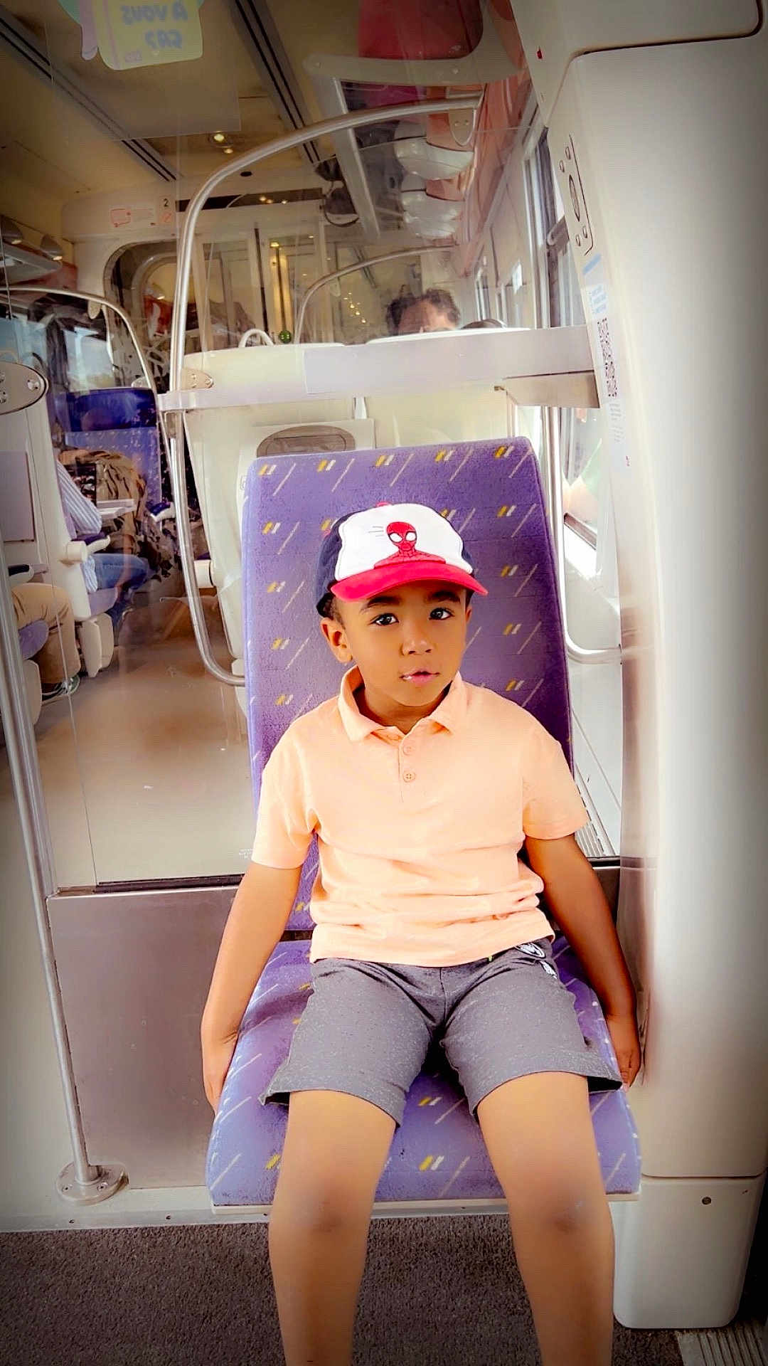 Bryan a rejoint le concours — aidez-le/la à gagner de superbes lots ! child, boy, train, seat, cap, spiderman, shorts, casual_clothing, indoor, public_transport, window, curious, sitting, purple_seat, young, person, travel, public_space, portrait, daylight