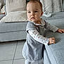 toddler, child, girl, standing, grey_dress, sofa, cushion, living_room, tile_floor, curious, long_sleeves, white_tights, indoors, plush, furniture, baby, person, home, cute, portrait