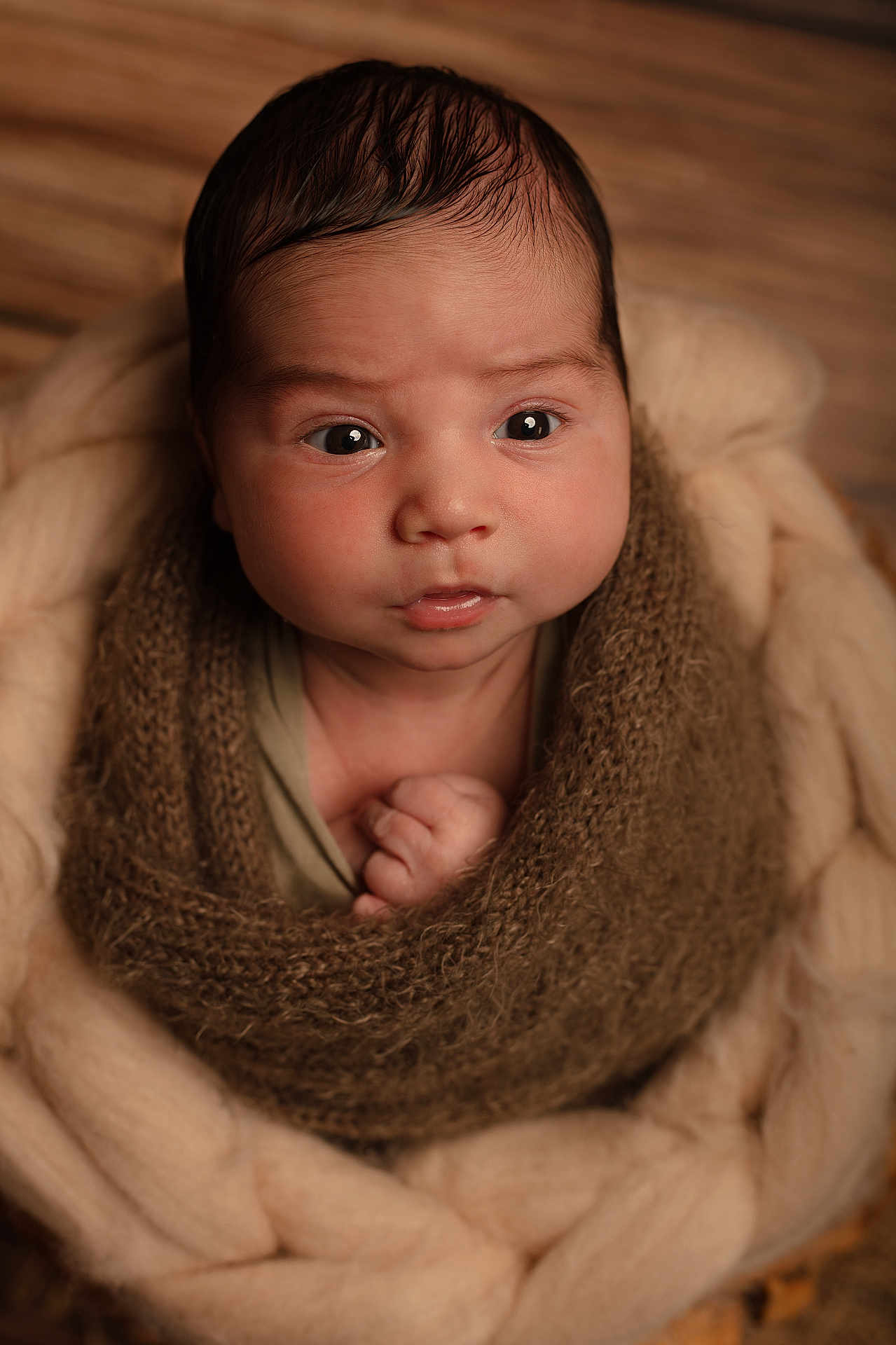 Numa a rejoint le concours — aidez-le/la à gagner de superbes lots ! baby, infant, face, expression, knitted_blanket, brown, cream, cozy, warm, cute, newborn, portrait, soft_texture, wrapped, child, hand, wood_background, indoor, closeup, young