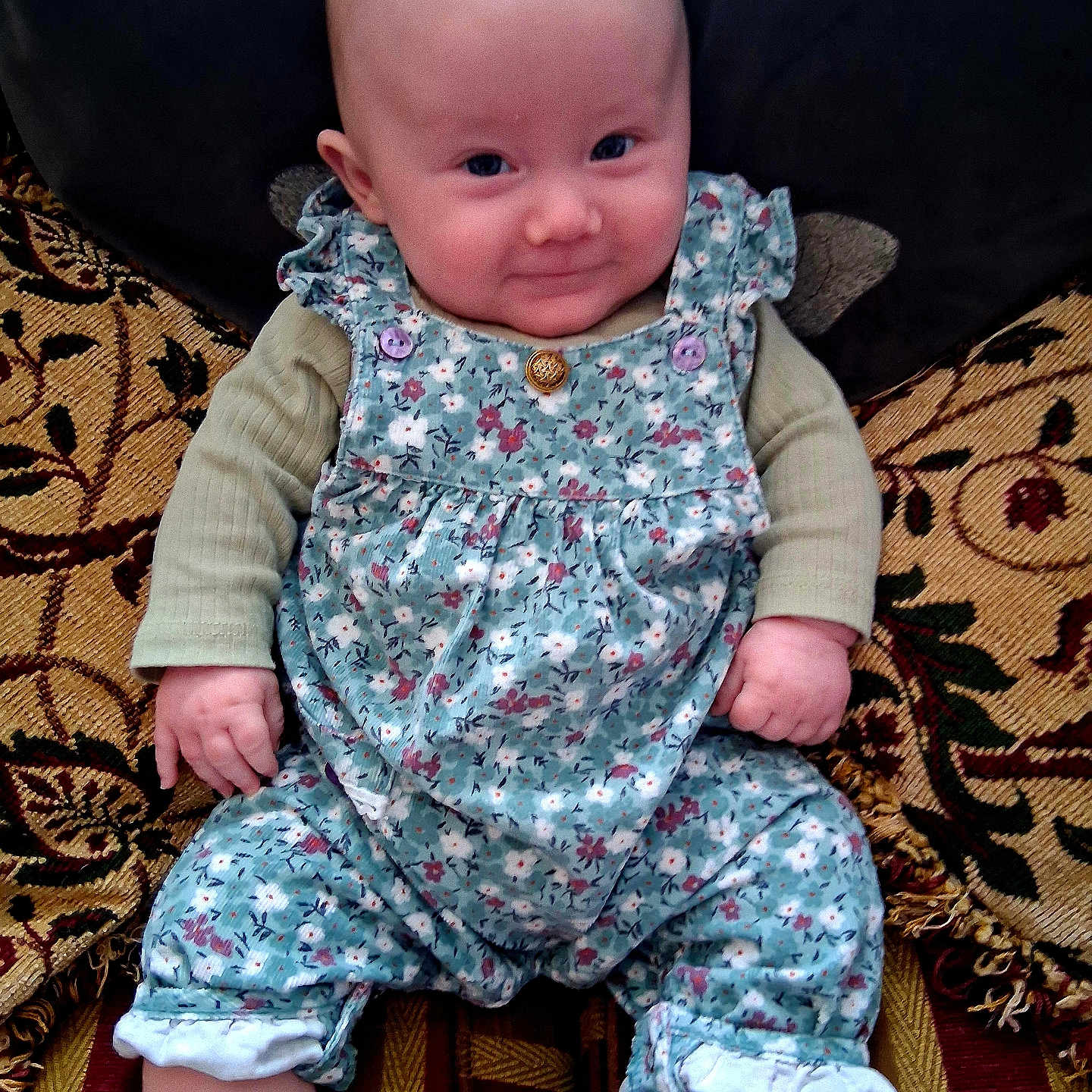 Lottie Button is registered to the contest to win money with this photo: baby, child, clothing, cozy, cushion, cute, face, floral_pattern, footwear, hand, happy, indoor, infant, patterned_fabric, person, portrait, romper, seated, smiling, socks