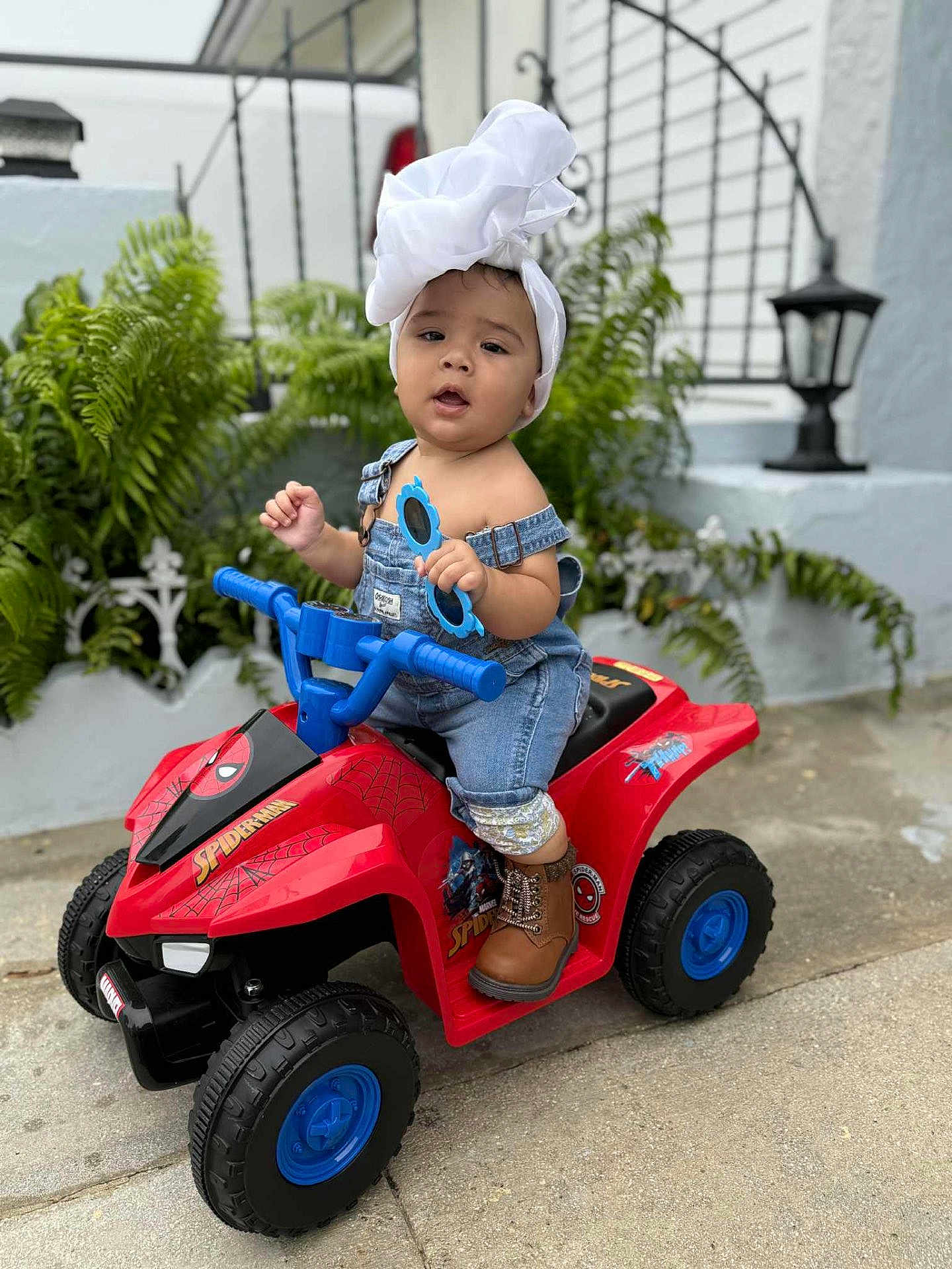 Alendy joined the competition — help win amazing prizes! toddler, child, toy, quad_bike, spiderman, outdoor, plants, headwrap, denim, overalls, sunglasses, boots, concrete, lantern, wall, greenery, face, person, play, cute