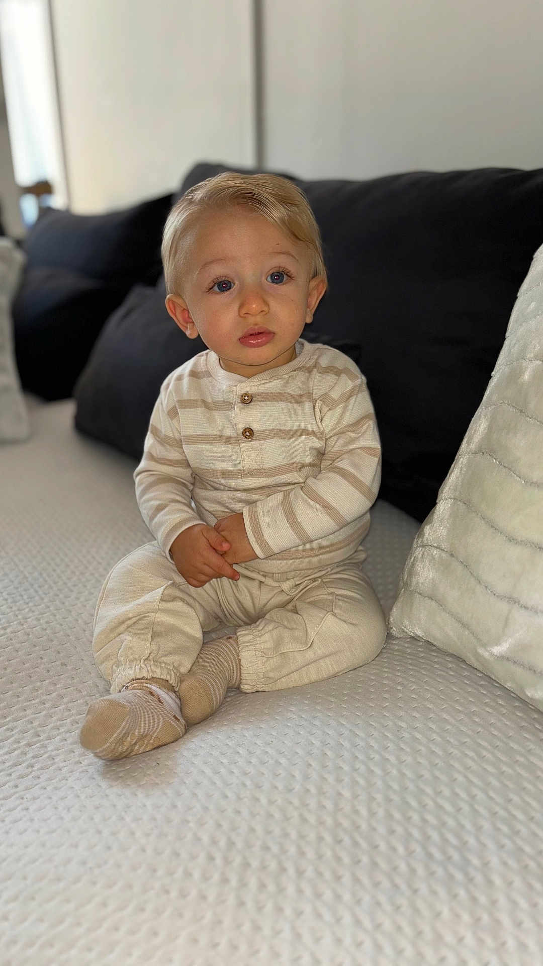 Sacha participe au concours pour gagner de l'argent avec cette photo : toddler, child, baby, sitting, couch, sofa, striped_clothing, beige, socks, blonde_hair, blue_eyes, indoor, home, pillow, soft_texture, curious_expression, young_child, portrait, cozy, comfortable
