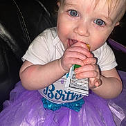 Arya is registered to the contest to win money with this photo: baby, child, tutu, purple, white_shirt, blue_eyes, snack_pouch, hands, face, curly_hair, sitting, black_leather, clothing, cute, portrait, indoor, young_child, chewing, nail, closeup