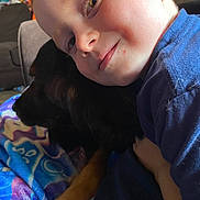 James joined the competition — help win amazing prizes! child, dog, cuddle, smile, face, blanket, blue_shirt, pet, indoor, cozy, happy, animal, friendship, comfort, closeup, portrait, young_child, furniture, relaxation, domestic