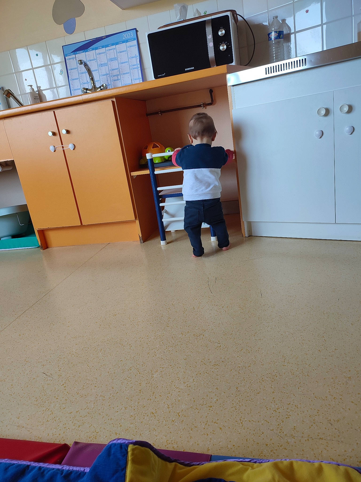 Lorenzo a rejoint le concours — aidez-le/la à gagner de superbes lots ! bookcase, building, cabinetry, carpet, chair, chest_of_drawers, cupboard, drawer, floor, flooring, hardwood, home_appliance, houseplant, kitchen, machine, person, refrigerator, room, shelf, shelving