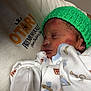 newborn, baby, sleeping, infant, green_hat, onesie, patterned_clothing, closeup, face, peaceful, cuddled, soft_light, human, child, portrait, cute, warm, resting, indoor, person