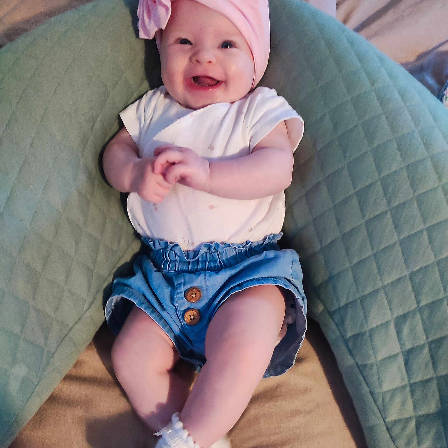 Tilelly participe au concours pour gagner de l'argent avec cette photo : baby, blue_shorts, child, comfortable, cute, flower, green_pillow, hands, happy, indoors, infant, legs, lying_down, pink_headwrap, quilted_pillow, small, smiling, socks, soft_lighting, white_shirt