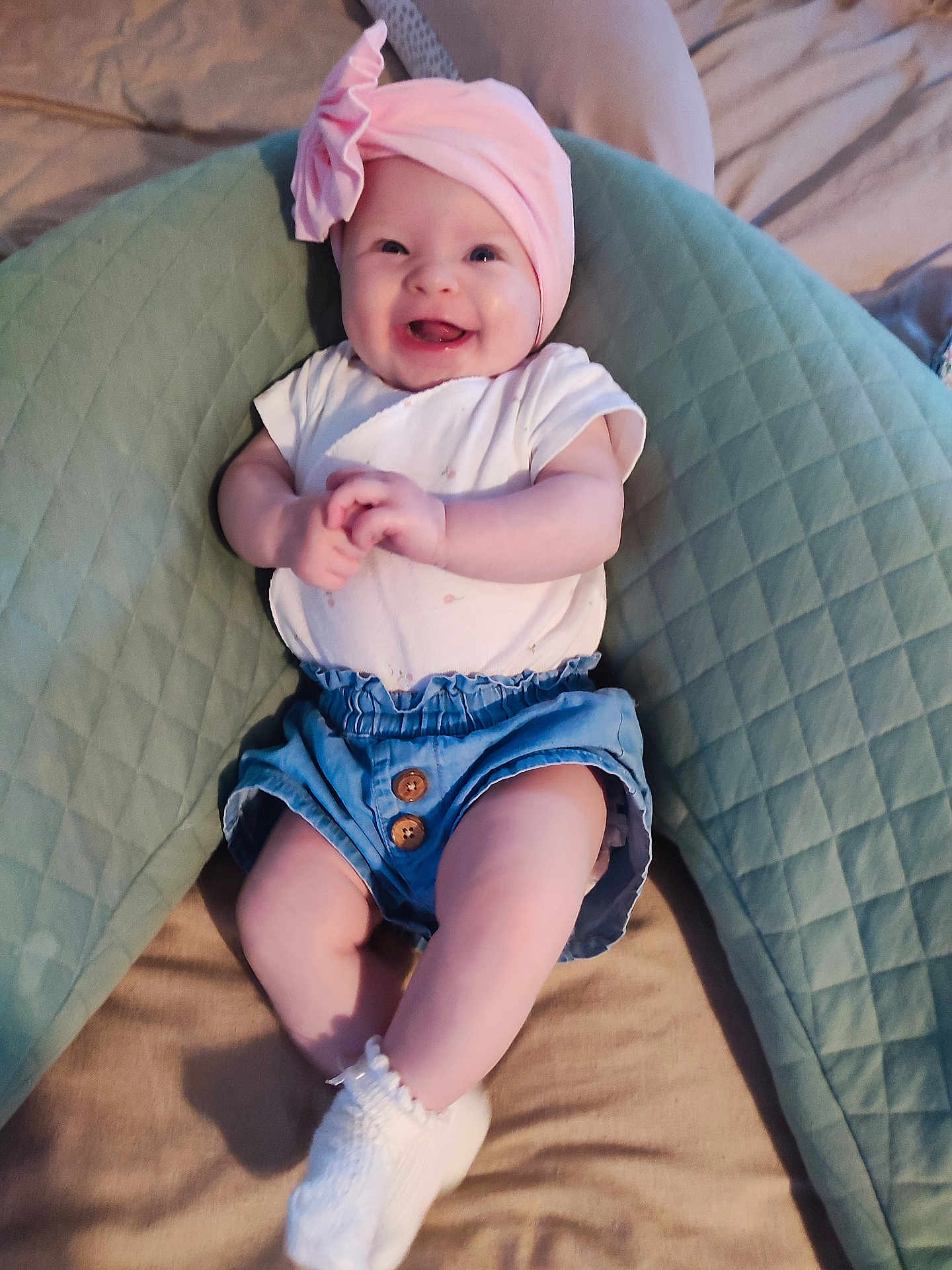 Tilelly participe au concours pour gagner de l'argent avec cette photo : baby, smiling, pink_headwrap, flower, white_shirt, blue_shorts, quilted_pillow, green_pillow, socks, infant, cute, happy, lying_down, indoors, child, soft_lighting, hands, legs, comfortable, small