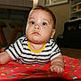 baby, child, infant, blue_eyes, striped_shirt, yellow_collar, quilt, floral_pattern, floor, indoor, furniture, curious, lying_down, skin, face, hand, arm, head, expression, home