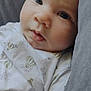 baby, infant, close_up, face, blue_eyes, white_clothing, patterned_clothing, hot_air_balloon, cushion, gray, soft_texture, indoors, portrait, young_child, cute, calm, curious, skin, head, person