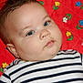 baby, child, blue_eyes, striped_shirt, red_quilt, flower_pattern, infant, cute, portrait, close_up, cheeks, lying_down, soft_skin, curious, young_child, head, face, hand, indoor, colorful_background