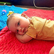Alexander is registered to the contest to win money with this photo: baby, infant, child, portrait, lying_down, wide_eyes, looking_at_camera, striped_clothing, blanket, red_blanket, blue_blanket, toy, hat, indoor, home, close_up, face, head, safe, colorful