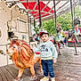 Mikaïl participe au concours pour gagner de l'argent avec cette photo : amusement_park, boy, cap, carousel, carousel_horse, casual_clothing, child, daylight, fun, jeans, outdoor, person, playful, red_and_white_canopy, ride, smiling, sneakers, toy_lion, trees, wooden_floor