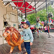 Mikaïl participe au concours pour gagner de l'argent avec cette photo : amusement_park, background_blur, boy, cap, carousel, casual_clothing, child, colorful, curious, daytime, fun, lion_statue, outdoor, park, person, playground, ride, sneakers, toy, wooden_floor