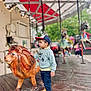 amusement_park, background_blur, boy, cap, carousel, casual_clothing, child, colorful, curious, daytime, fun, lion_statue, outdoor, park, person, playground, ride, sneakers, toy, wooden_floor