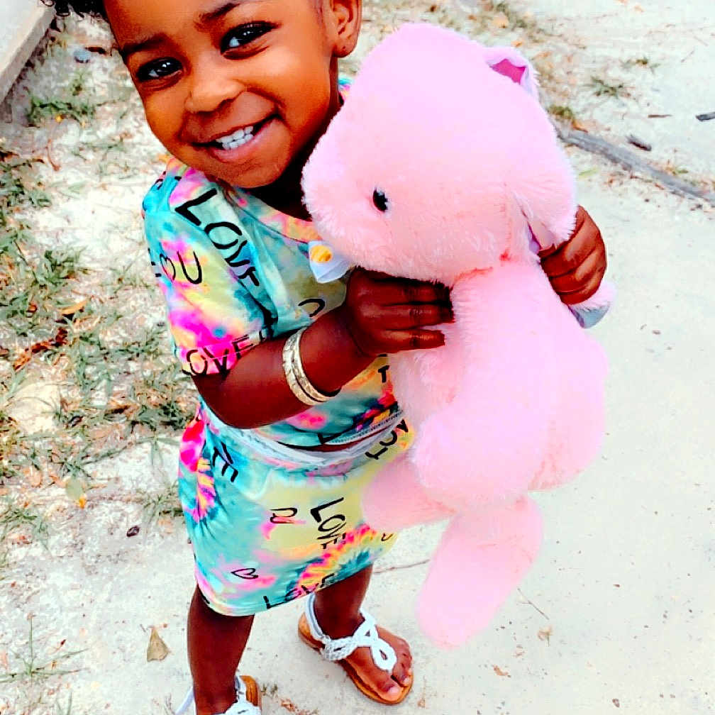 Kamiyah is registered to the contest to win money with this photo: child, clothing, dress, face, female, footwear, girl, grass, happy, head, outdoors, person, photography, plant, portrait, sandal, shoe, shorts, smile, teddybear