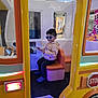 child, boy, sunglasses, hoodie, play_bus, indoor, smiling, seat, pretending, toy, play_area, colorful, casual_clothing, blue_shoes, fun, happy, leisure, kid, playing, pretend_play