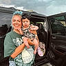 baby, black_car, blue_hair, car, casual_clothing, child, cloudy_sky, facial_expression, headband, holding, jeans, nature, open_car_door, outdoor, pearl_necklace, person, portrait, smile, tshirt, woman