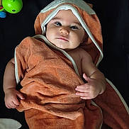 Jeannette is registered to the contest to win money with this photo: baby, towel, hood, toy, child, infant, cute, lying_down, orange, soft_texture, blanket, plaything, smiling, face, hand, skin, indoors, comfort, rest, young