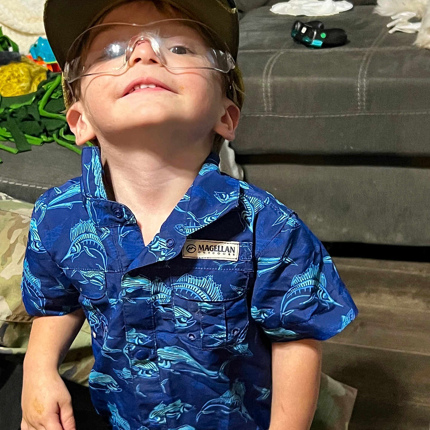 Karson joined the competition — help win amazing prizes! blue_shirt, boy, cap, casual, child, couch, curious, cute, fish_pattern, floor, glasses, indoor, person, playful, portrait, short_sleeve, smile, standing, toy, young