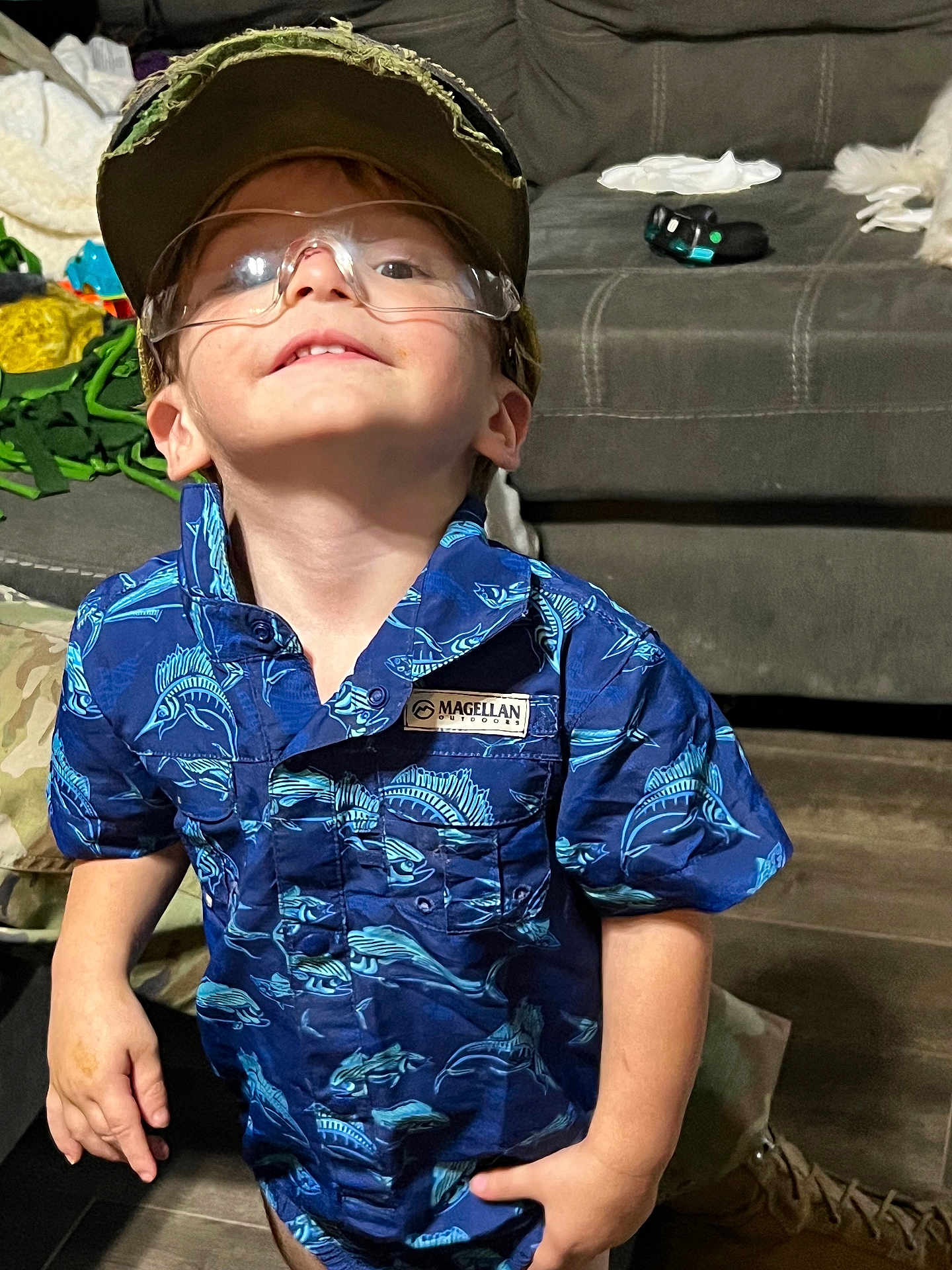Karson joined the competition — help win amazing prizes! child, boy, glasses, cap, blue_shirt, fish_pattern, indoor, couch, toy, smile, short_sleeve, person, floor, casual, young, curious, standing, portrait, cute, playful